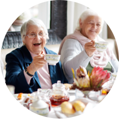 Two senior women enjoying tea in a bright and cozy living space with food on the table.