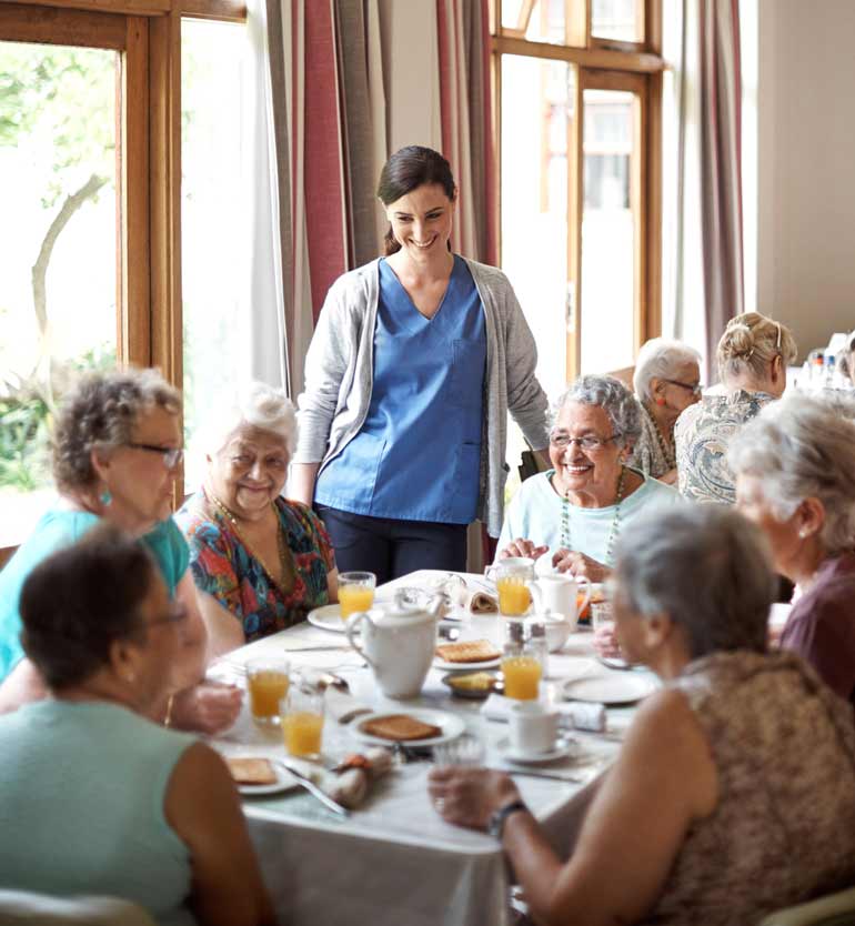 A group of senior women dining together in a bright assisted living community dining room.