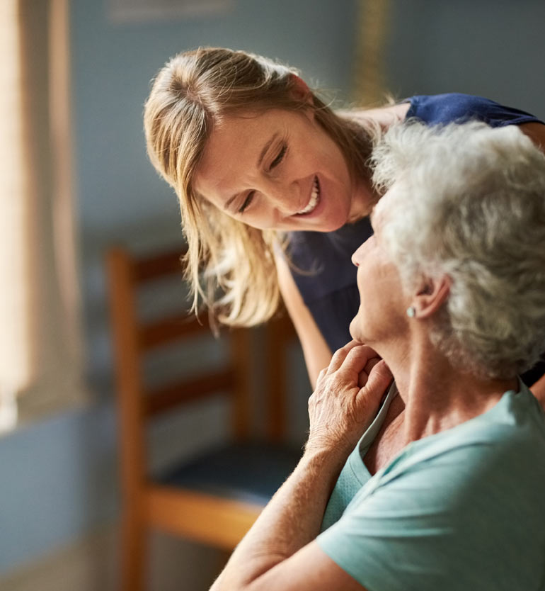 Caregiver smiling and interacting with a senior woman in a memory care unit.