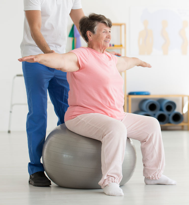Elderly woman exercising with the help of a therapist on a stability ball.