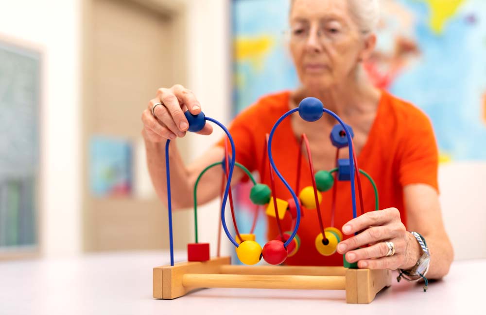 Senior woman engaging in a memory care activity with a colorful bead maze at a senior living unit.