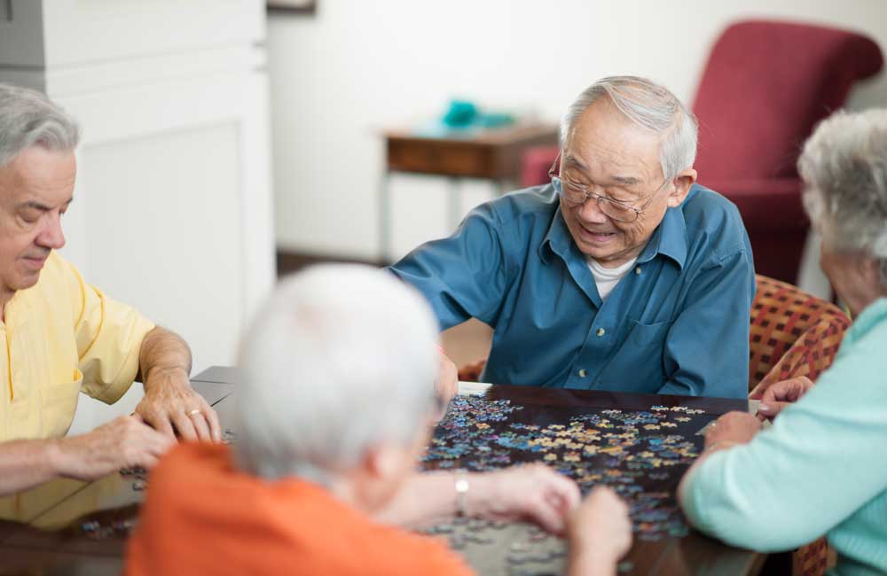 Elderly residents working together on a puzzle at a shared table in a living space.
