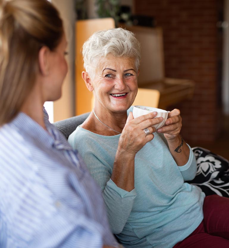Senior woman enjoying a conversation with a team member at a living community while holding a cup.