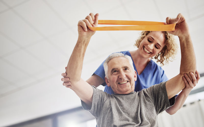 Senior man with a physical therapist doing an exercise with a resistance band in a wellness center.